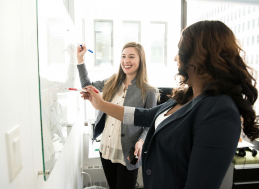 2 Women Standing in Front of a Whiteboard